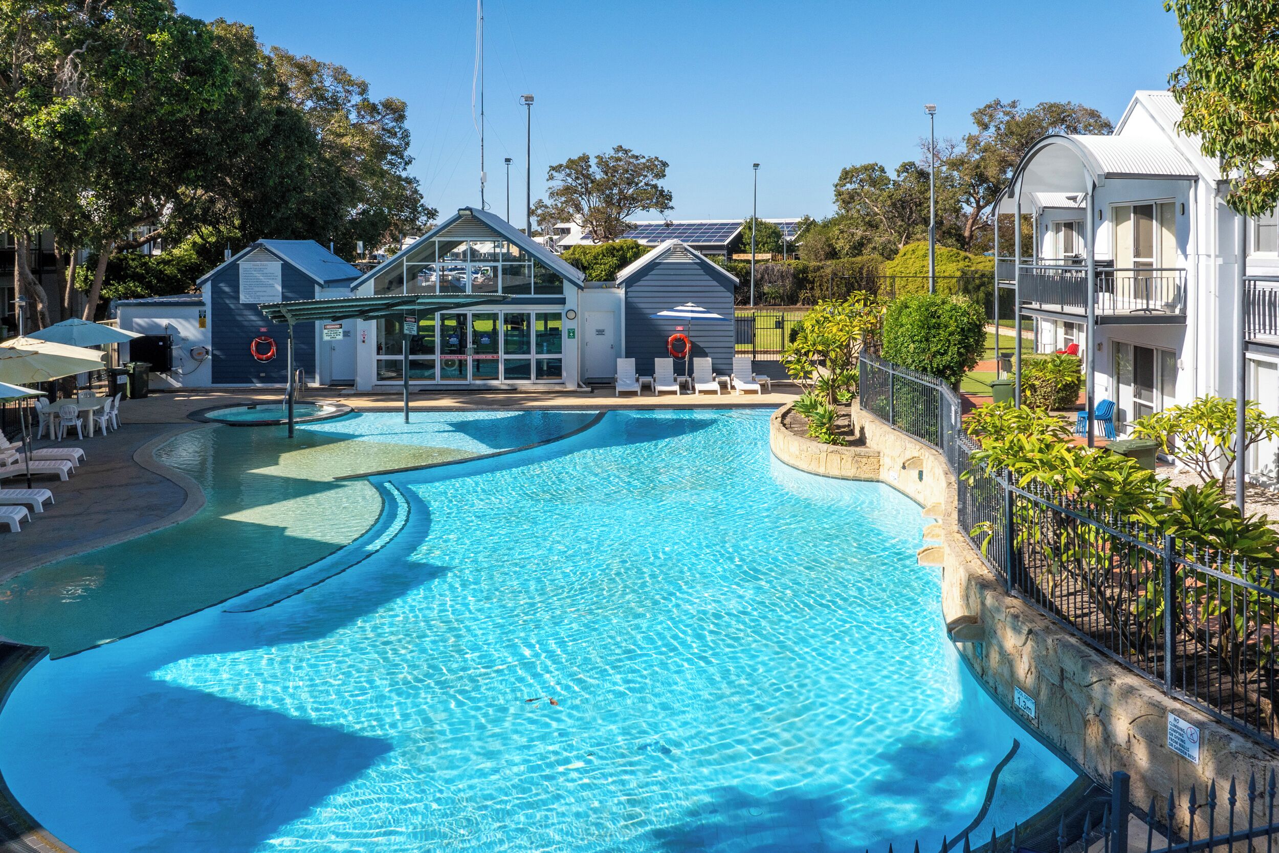 A swimming pool with a curved design, surrounded by lounge chairs and a building with a glass facade.