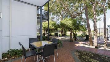 Eine Terrasse im Freien mit Tisch und Stühlen, umgeben von Bäumen und einem Pflasterweg.