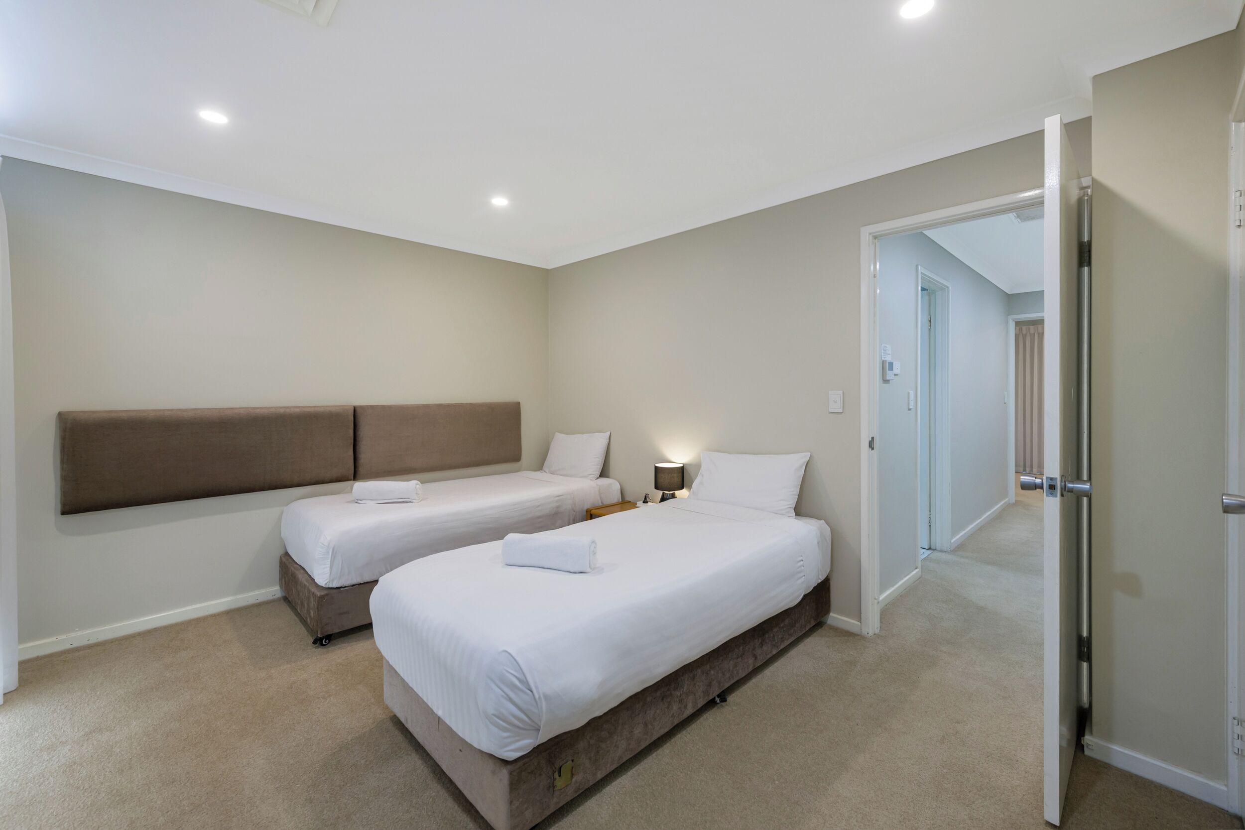 A hotel room with two beds, a headboard, a nightstand, and a lamp.