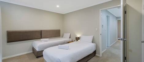A hotel room with two beds, a headboard, a nightstand, and a lamp.