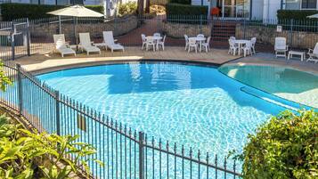 A swimming pool with a metal fence, surrounded by white lounge chairs and tables.