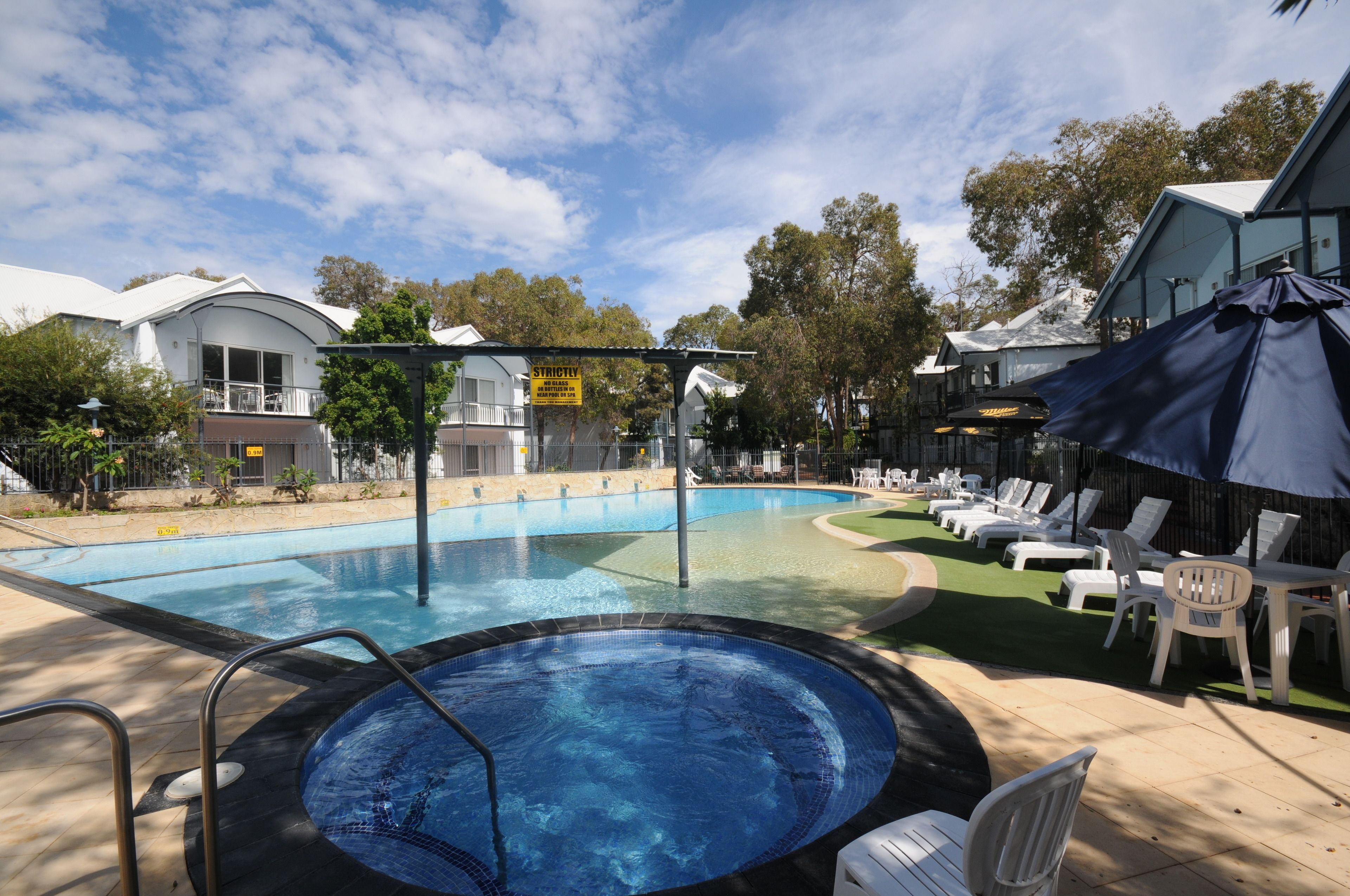 A swimming pool with a hot tub, lounge chairs, and umbrellas.