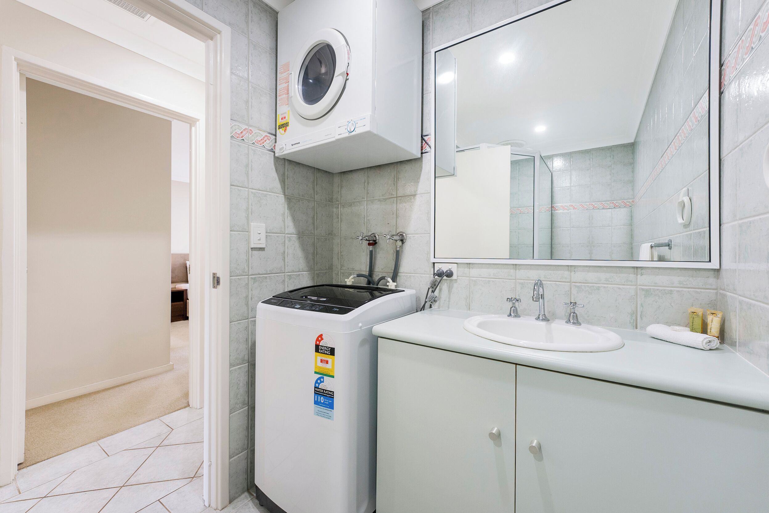 Une salle de bain moderne équipée d’un lave-linge, d’un lavabo et d’un miroir.