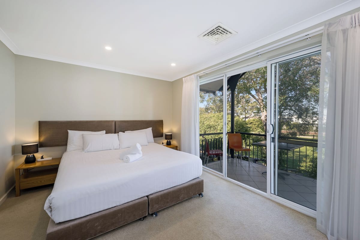 A bedroom with a large bed, a nightstand, a lamp, and a sliding glass door leading to an outdoor area.