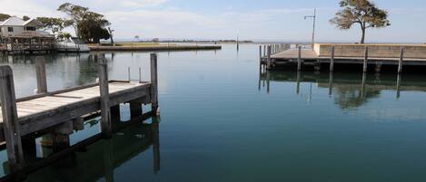 A calm waterfront with a wooden dock extending into the water, a small pier, and a tree on the right.