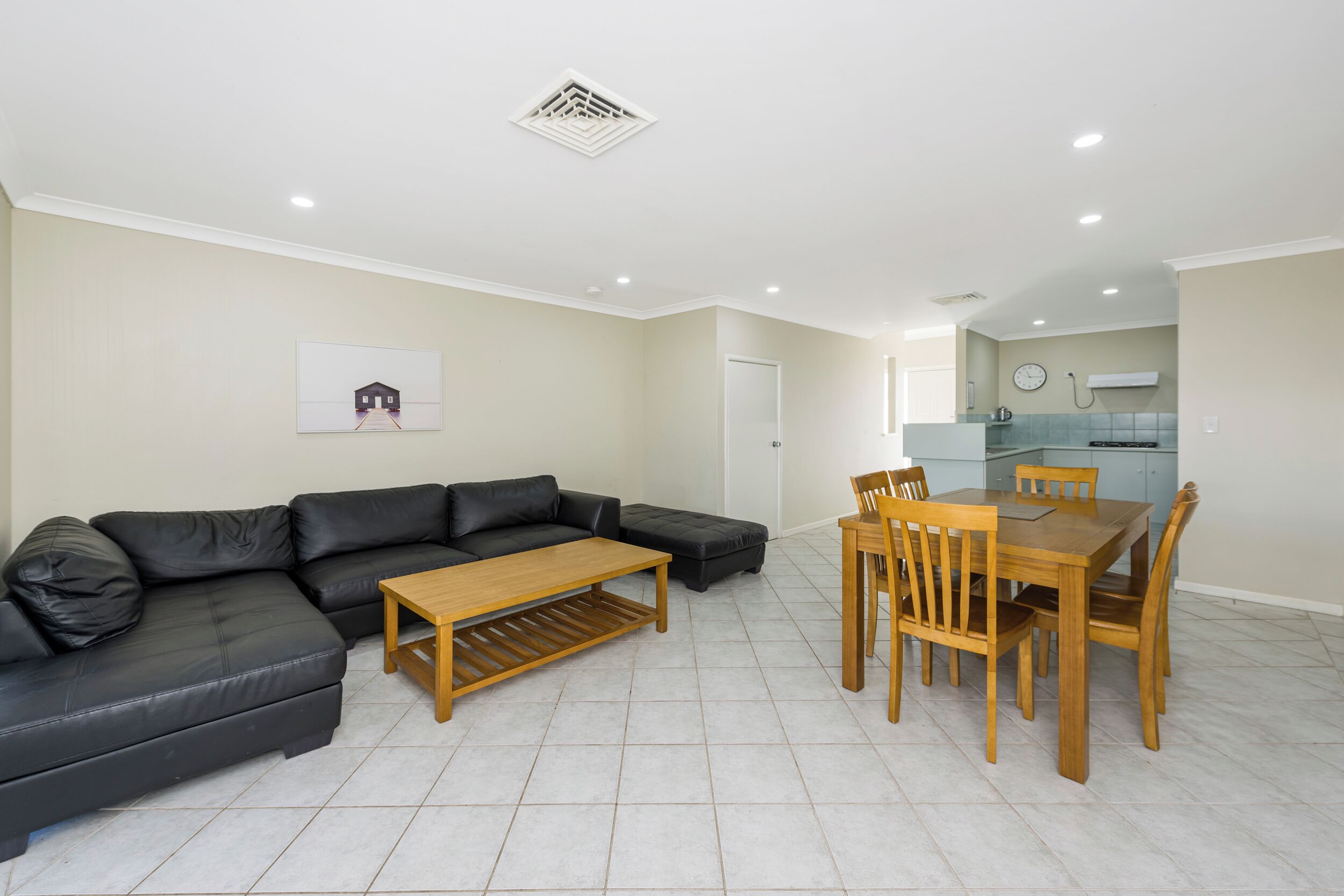 A modern living room with a sectional sofa, a wooden coffee table, and a dining area with a wooden table and chairs.