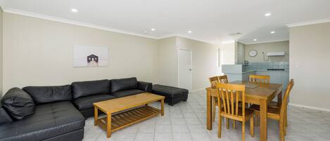 A modern living room with a sectional sofa, a wooden coffee table, and a dining area with a wooden table and chairs.