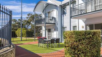 A modern building with a balcony, a paved patio, and a well-maintained lawn.