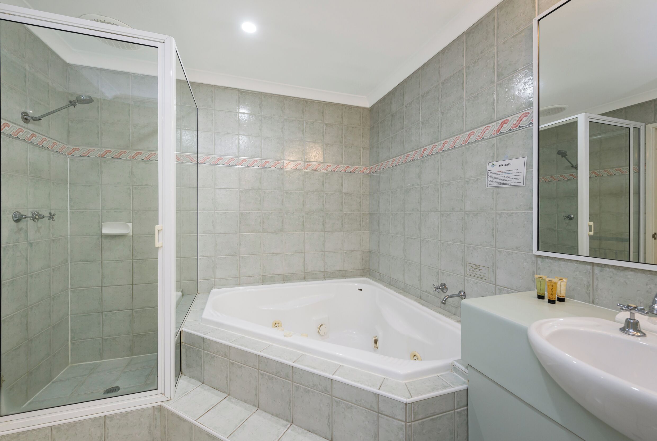 Un baño con ducha de vidrio, una bañera independiente y un lavamanos con artículos de aseo.
