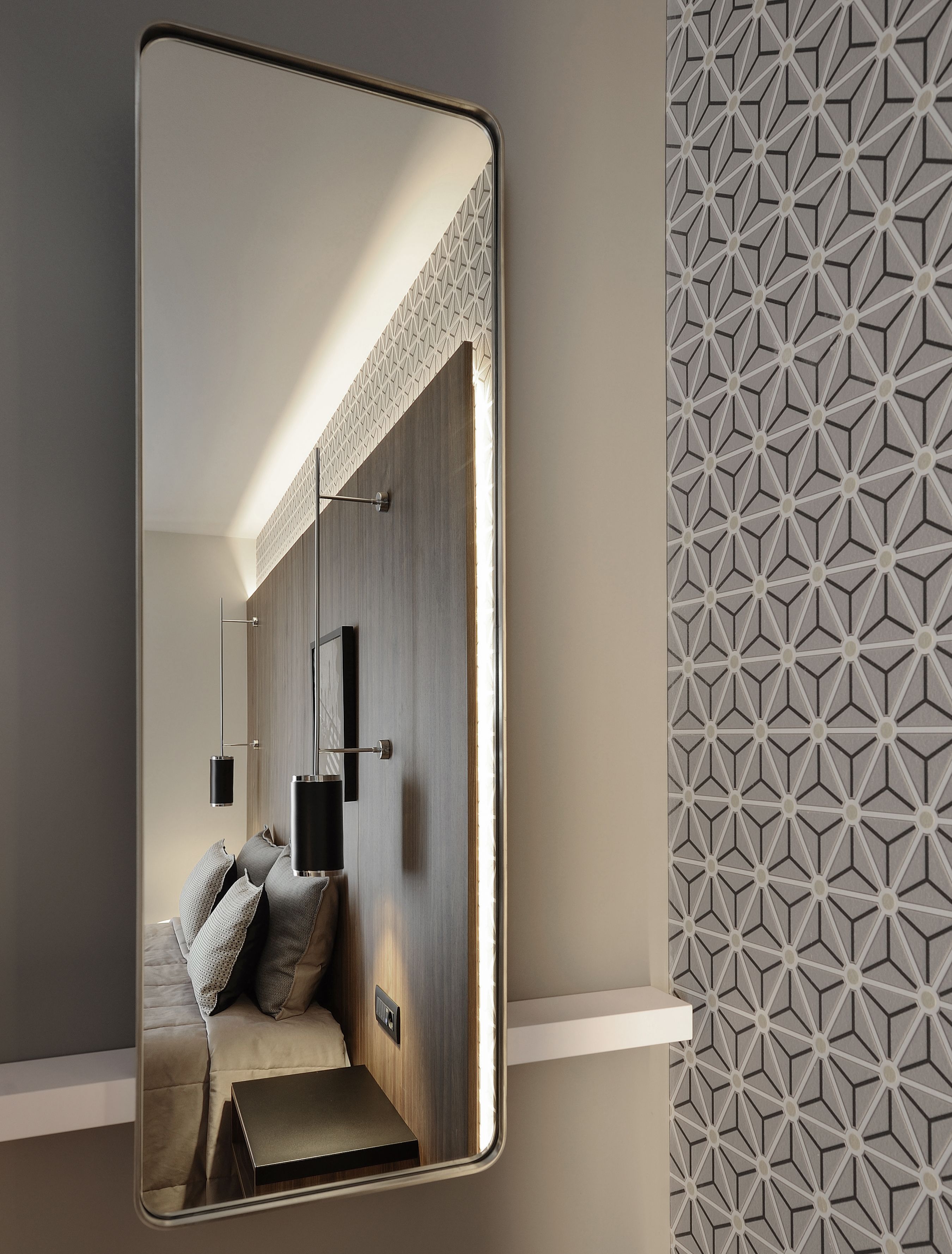 A modern bedroom with a large mirror, a bed with pillows, a bedside table, and a geometric-patterned wall.