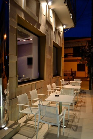 An outdoor seating area with white tables and chairs, a large mirror, and a view of the interior. - Evridiki (Kilkis)