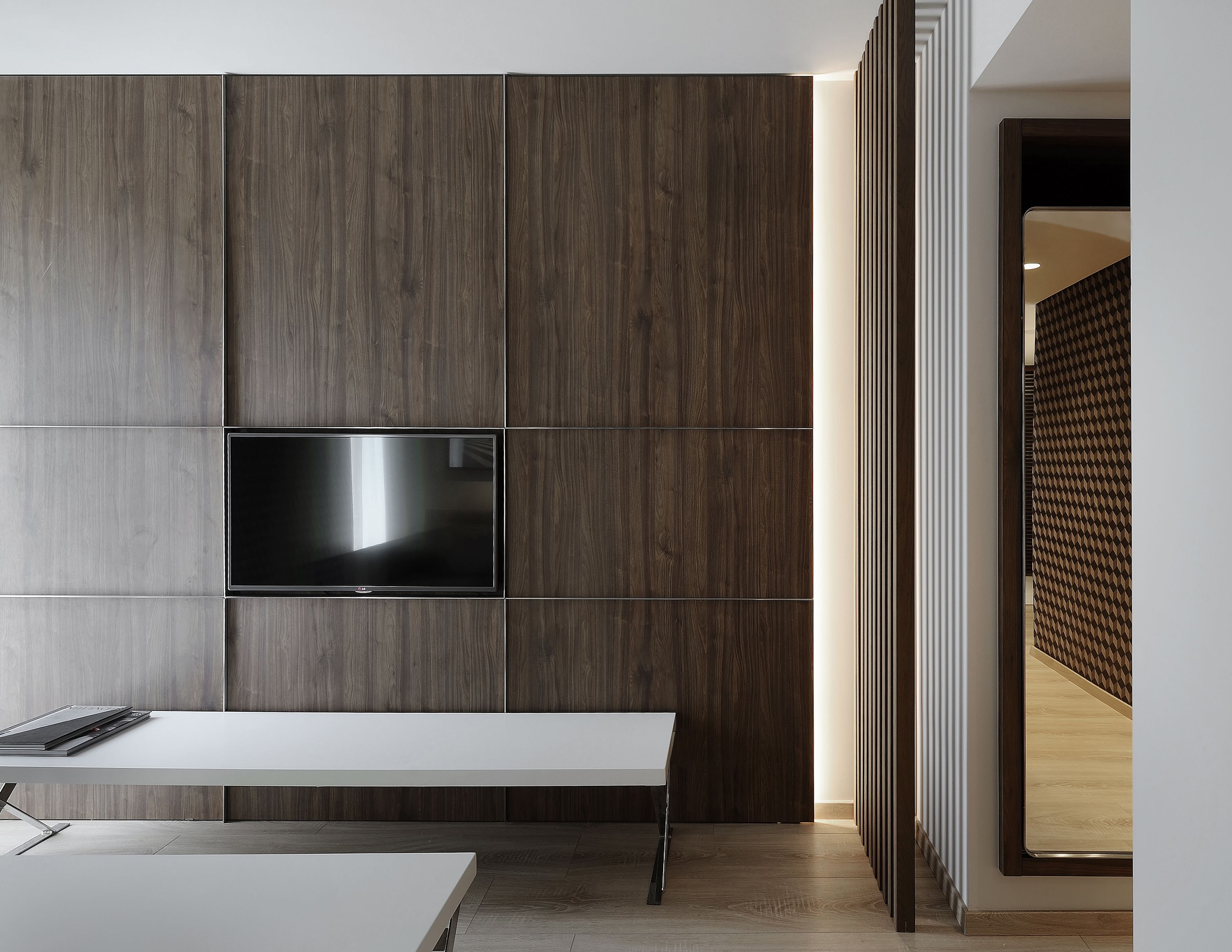 Une chambre moderne avec un téléviseur à écran plat fixé sur un mur en panneaux de bois, un bureau blanc et un séparateur à motifs.