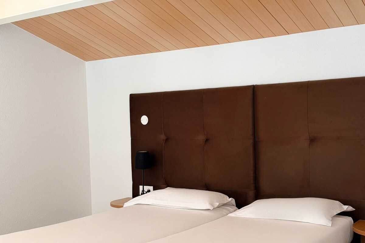 A double bed with a wooden headboard, a bedside table with a lamp, and a tiled floor.