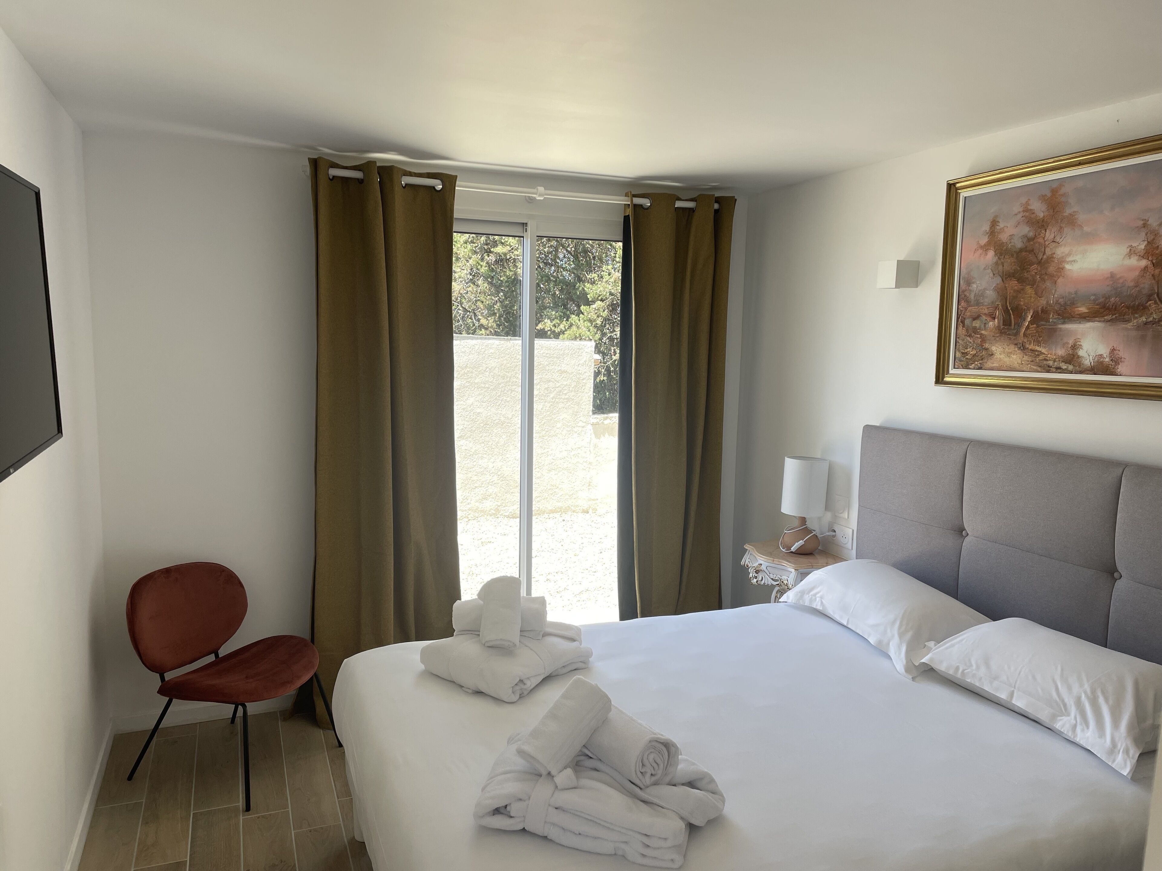 A hotel room with a bed, a chair, a painting, and a view of the outdoors.