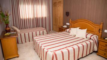 A hotel room with two beds, a wooden wardrobe, a bedside table with a lamp, and a potted plant.