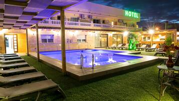 Un hotel con piscina, sillones de exterior y un patio bien iluminado.