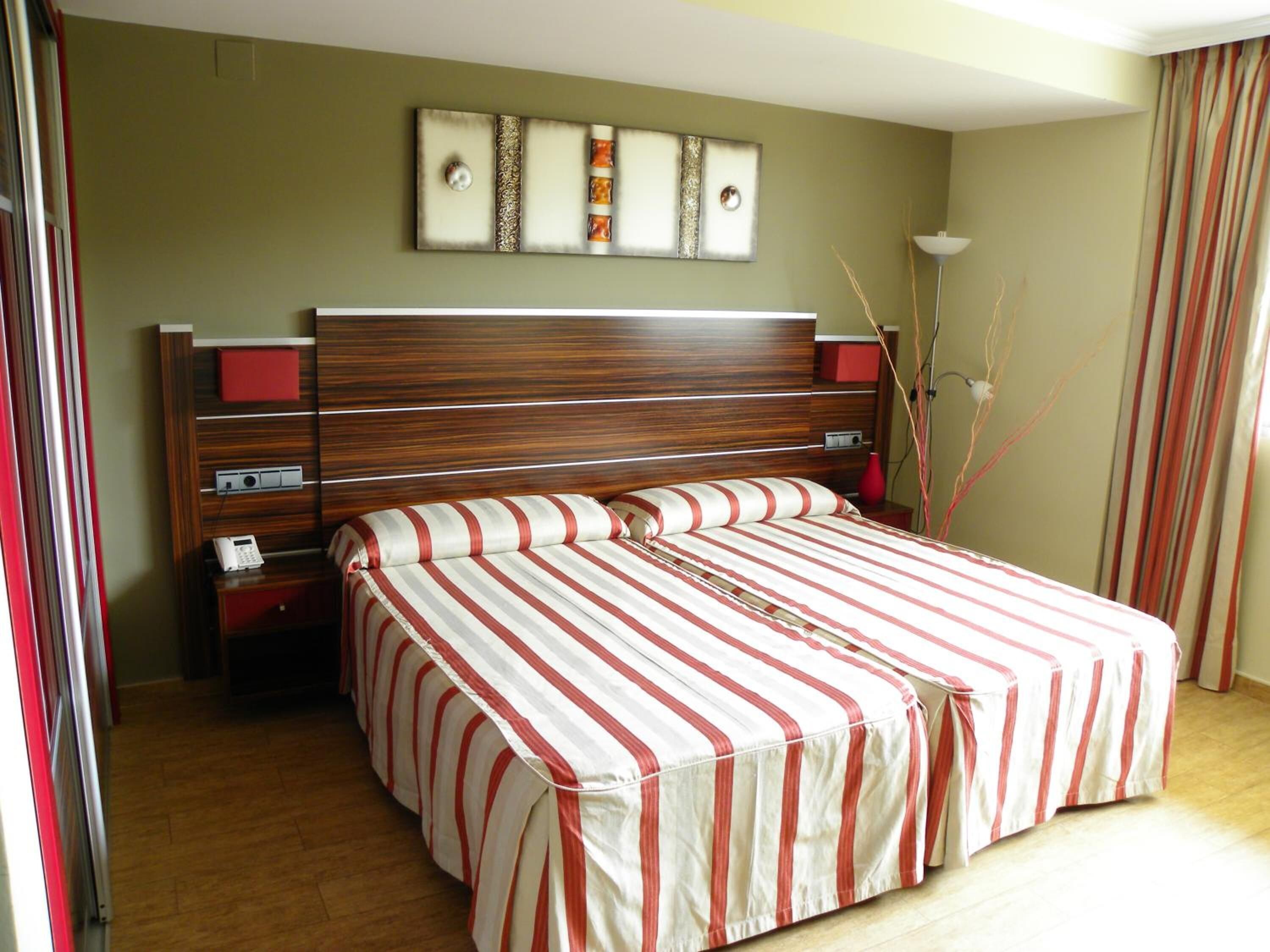 A hotel room with a large bed, a wooden headboard, a bedside table with a phone, and a wall art piece above the bed.
