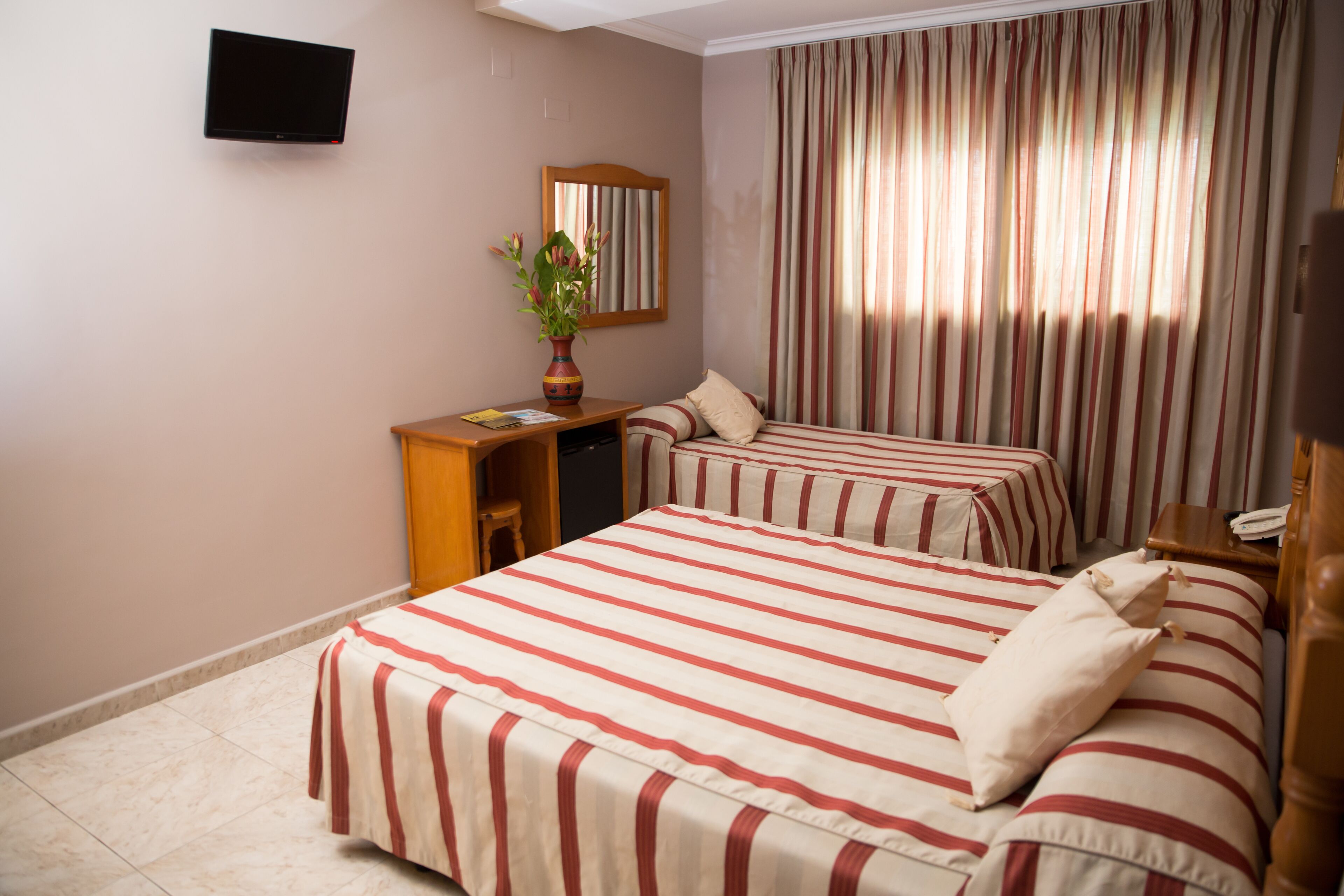 Ett hotellrum med två sängar, ett skrivbord, en stol, en tv och ett fönster med gardiner.