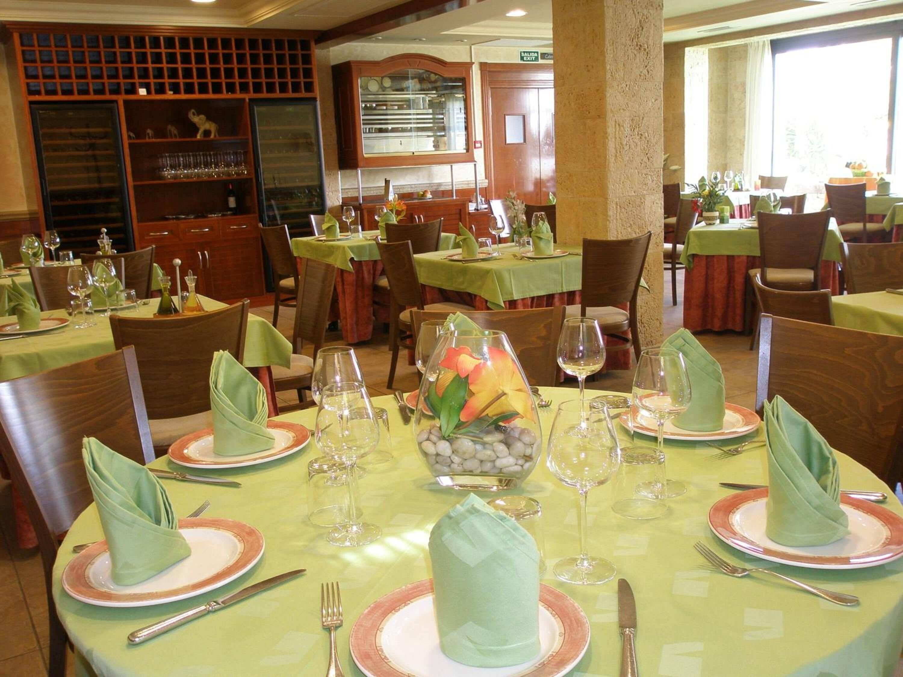 A restaurant with round tables set for dining, featuring green tablecloths, neatly folded napkins, and wine glasses.