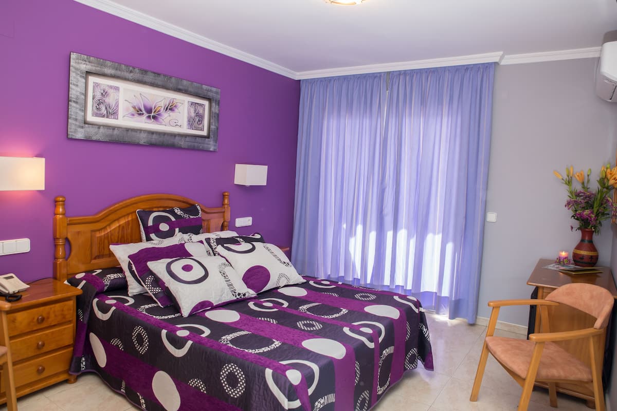 Une chambre à coucher comprenant un lit, une table de chevet, une chaise, un bureau et une fenêtre avec des rideaux.