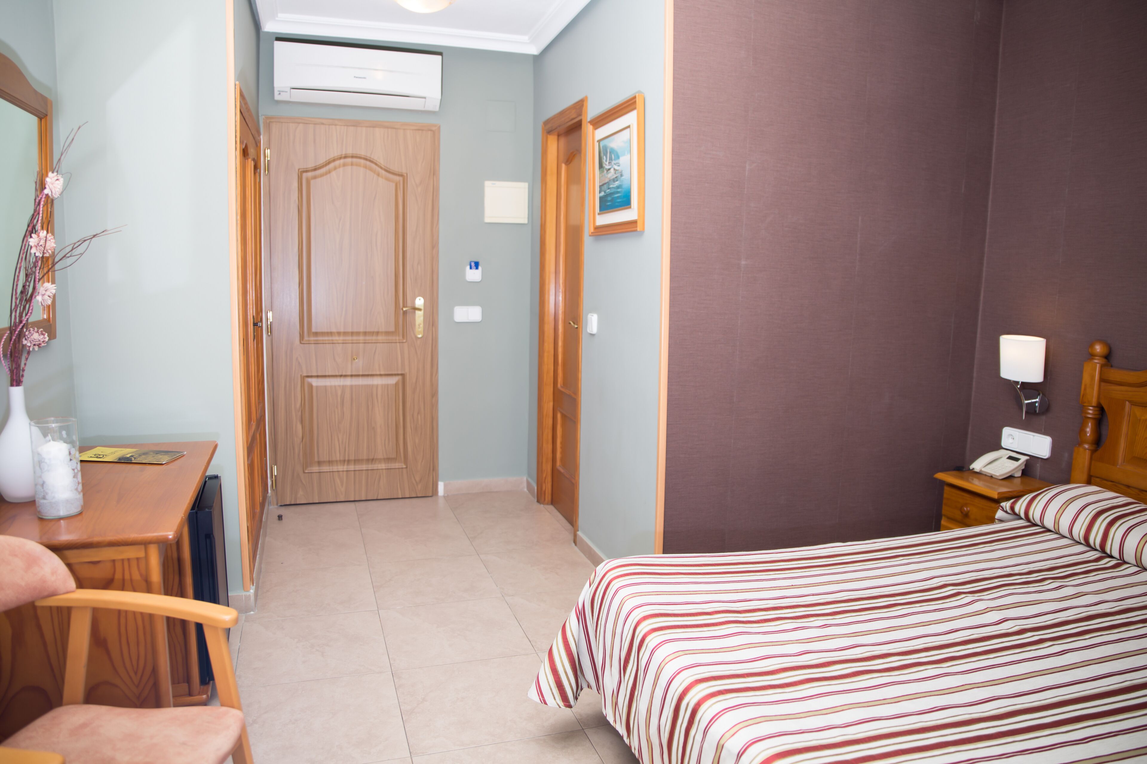 Une chambre d’hôtel équipée d’un lit, d’un bureau, d’une chaise, d’une table de chevet, d’une lampe et d’un téléphone fixé au mur.