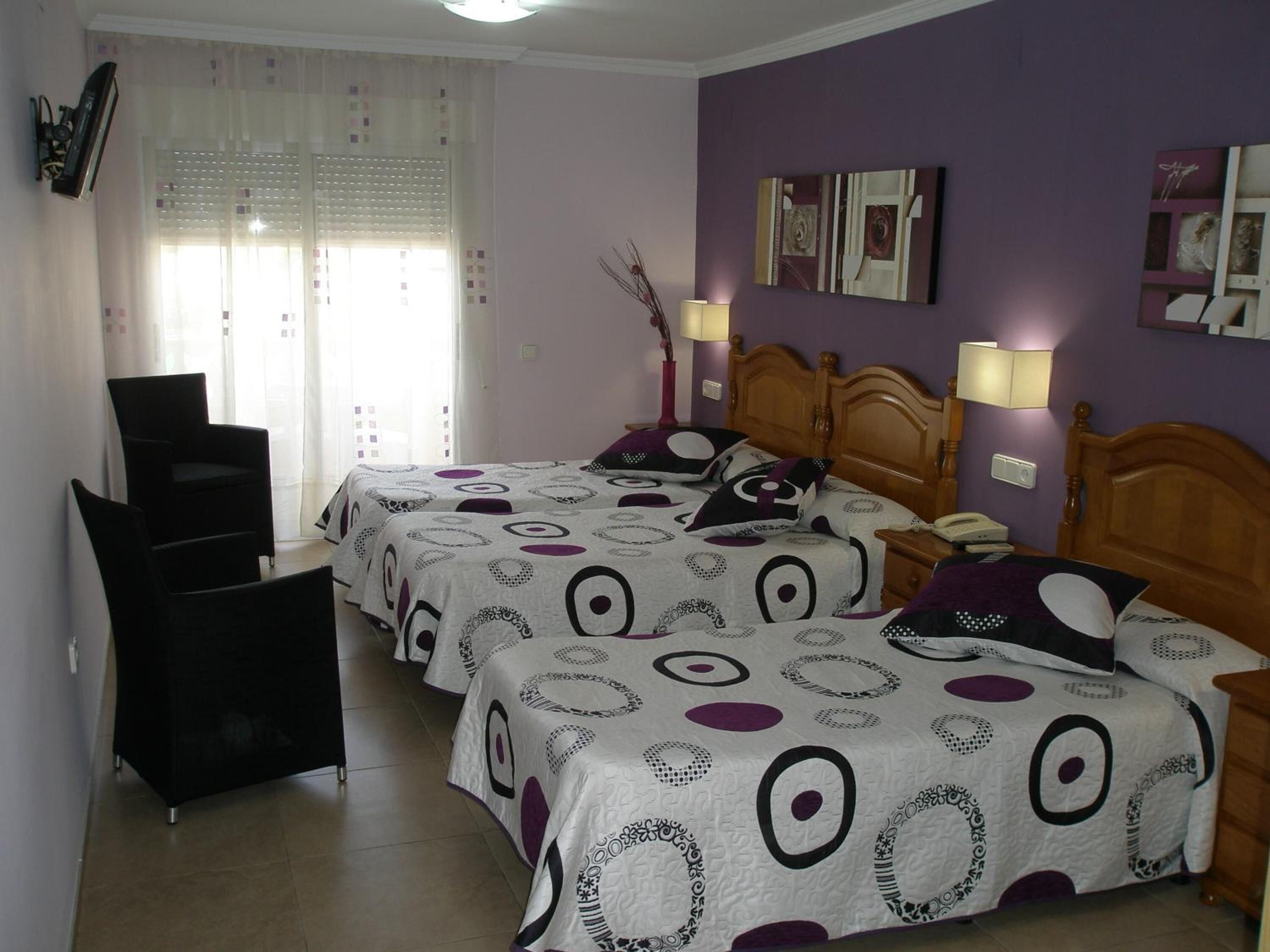 A bedroom with two beds, a chair, and a bedside table with a lamp.