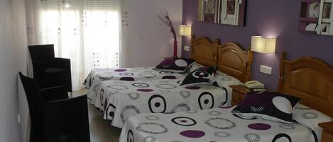 A bedroom with two beds, a chair, and a bedside table with a lamp.
