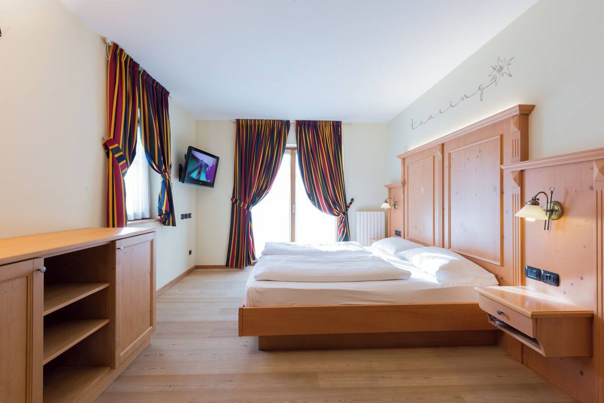 A bedroom with a bed, wooden wardrobe, and a TV on the wall.