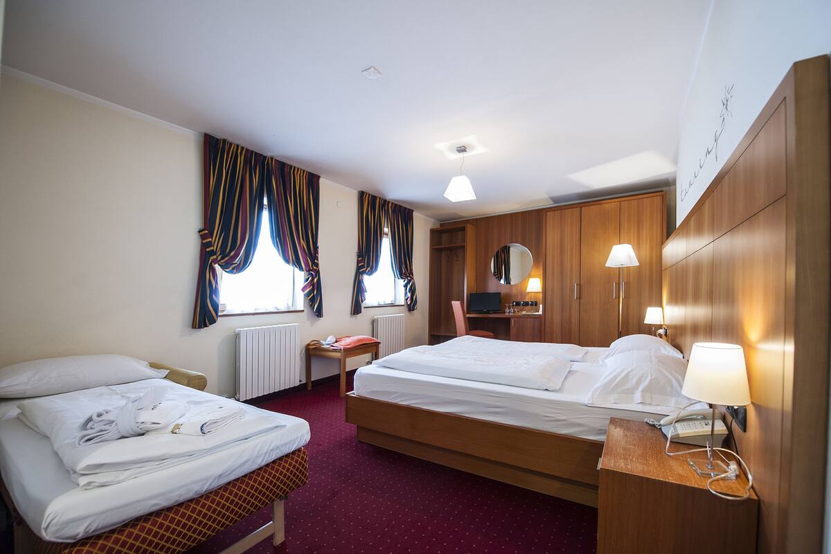 A hotel room with two beds, a desk with a lamp, a mirror, and a television.