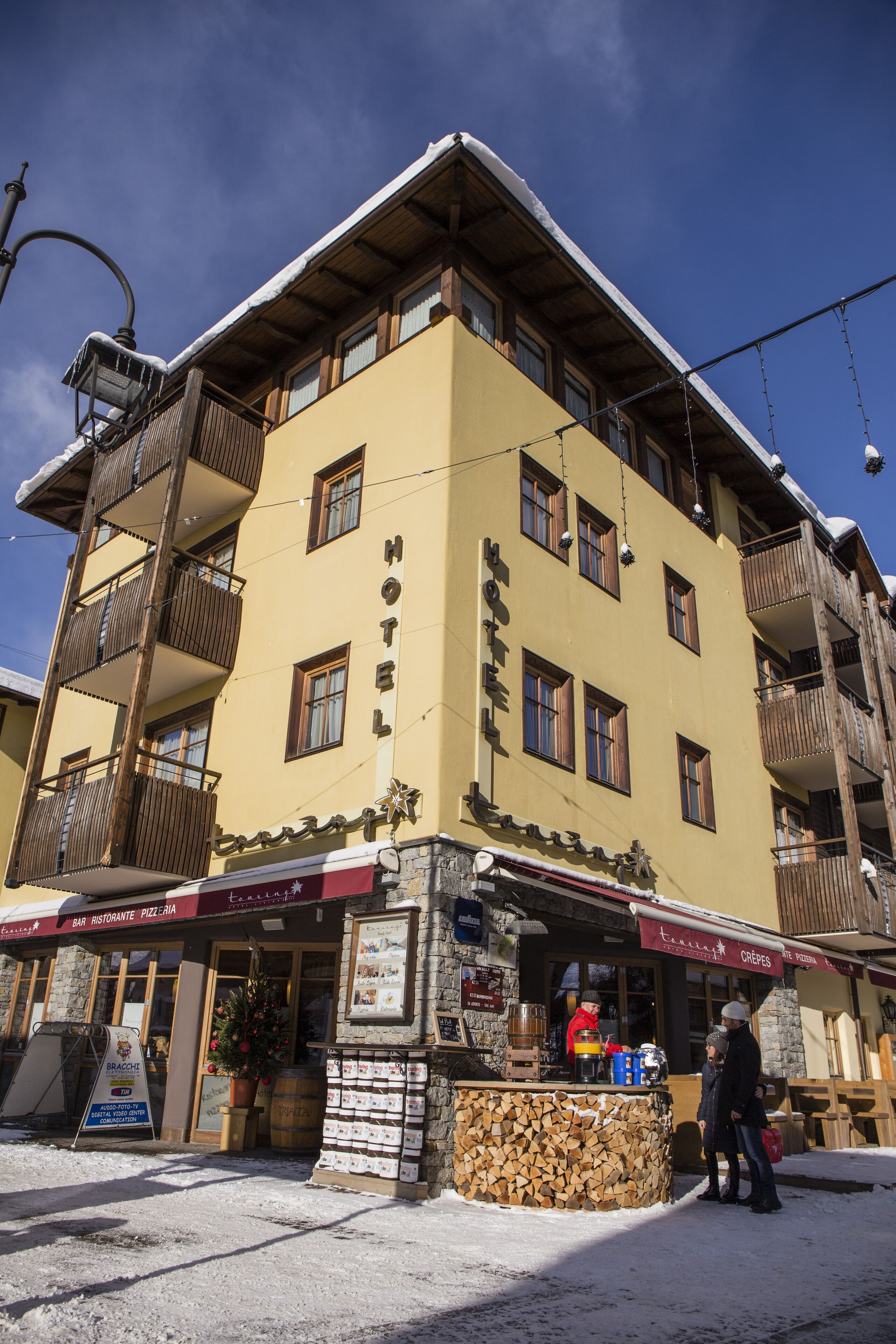 Un hotel con fachada amarilla, balcones y un bar en la planta baja.