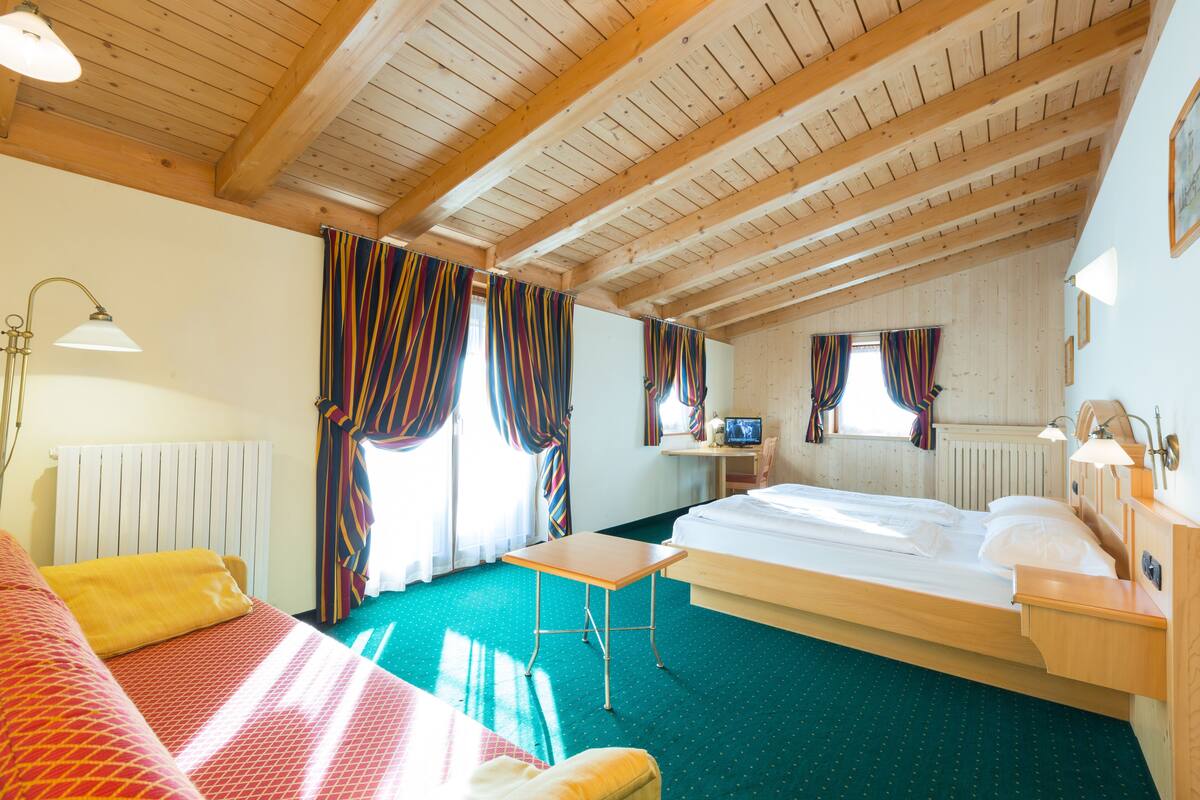 A hotel room with a wooden ceiling, a bed, a desk, and a TV.