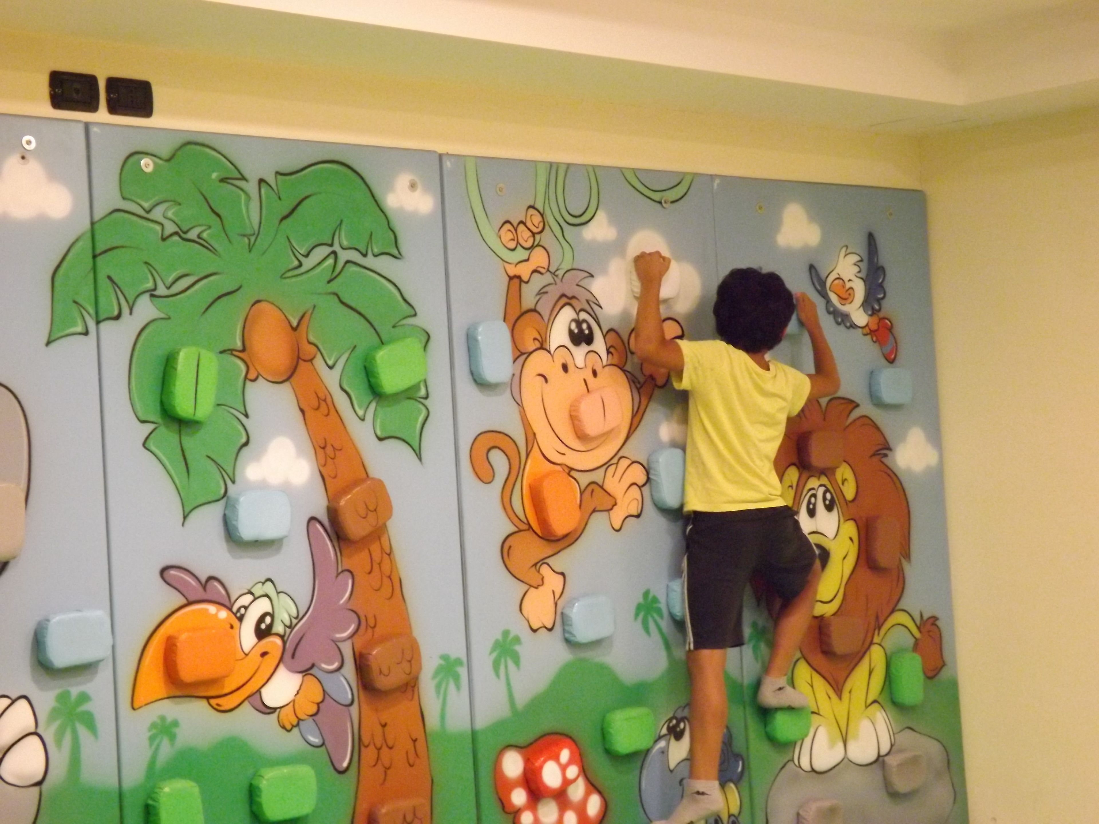 A child interacting with a wall mural featuring cartoon animals and a tree.