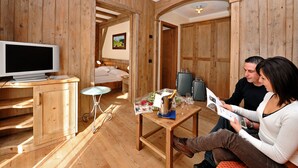 A wooden interior with a bed, a table with a bottle, glasses, and a magazine, and a television on a stand. - Hotel Touring Livigno (Livigno)