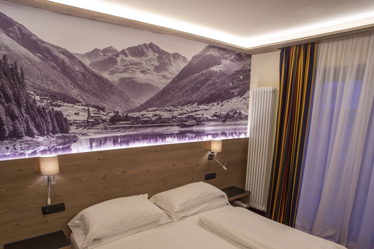 A hotel room with a bed, a nightstand, a lamp, a wall-mounted TV, and a window with curtains.