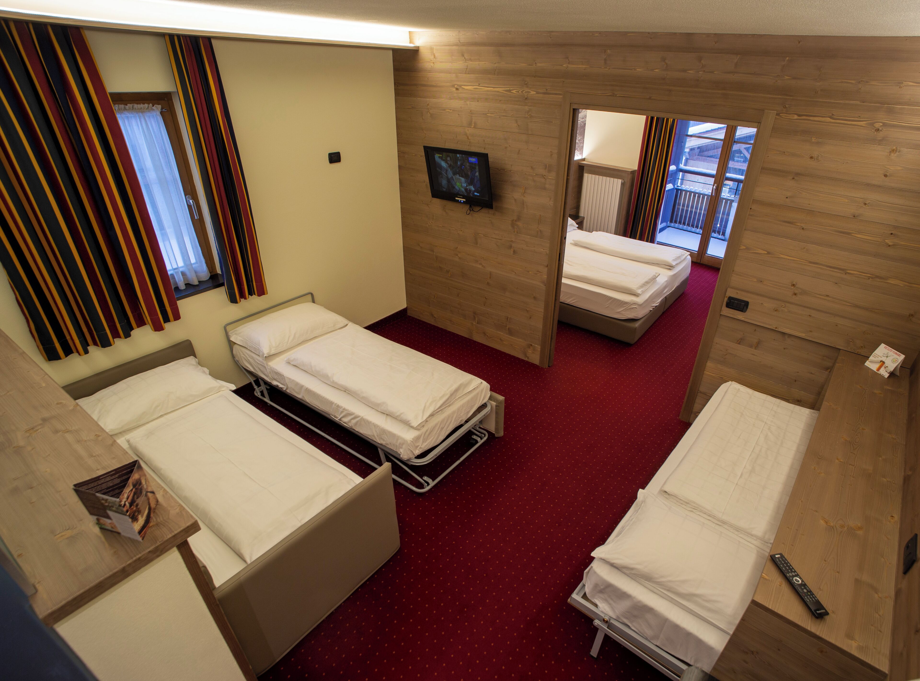 A hotel room with three single beds, a television on the wall, and a window with curtains.