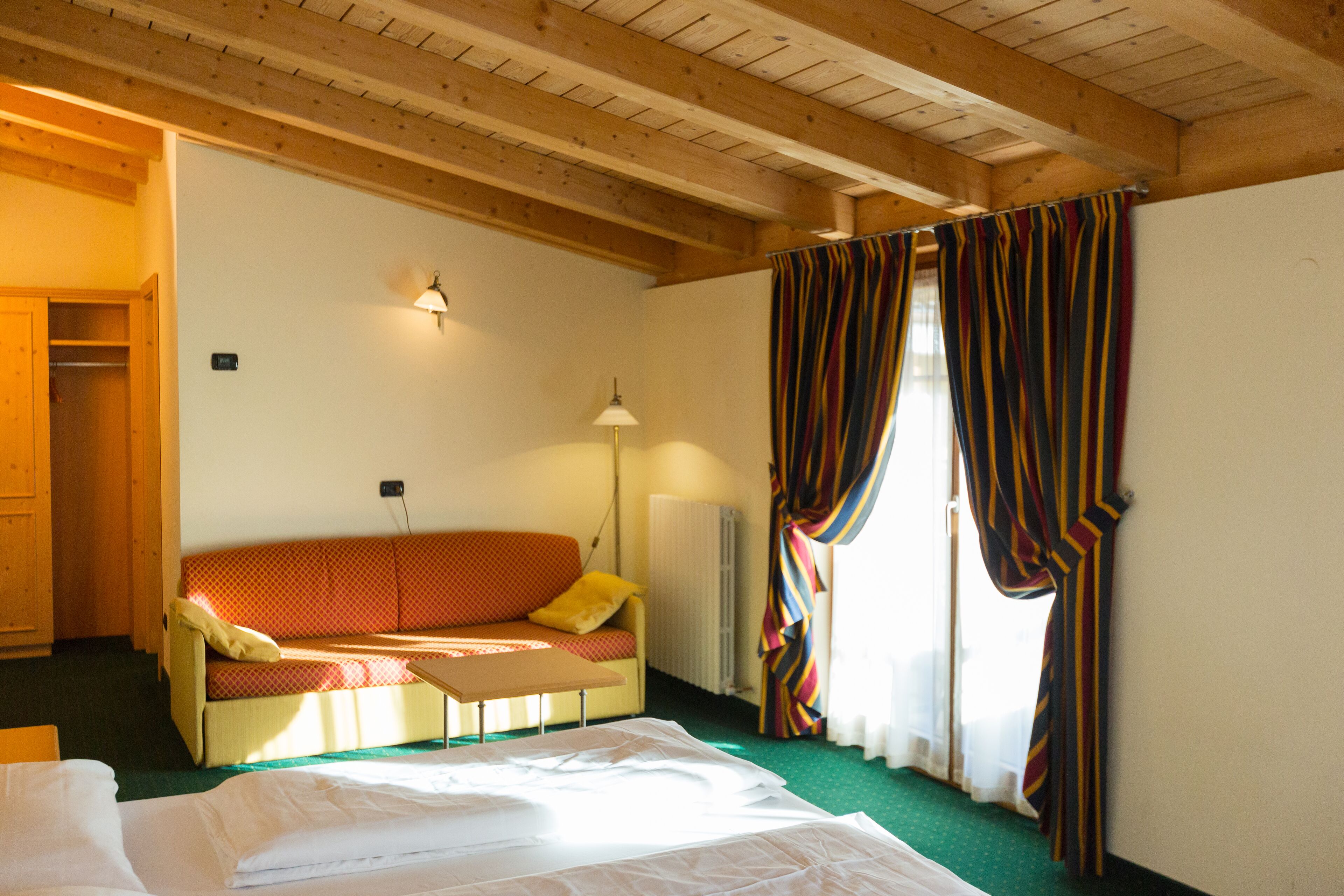 Una habitación con cama, sofá, mesa, lámpara y ventana con cortinas.