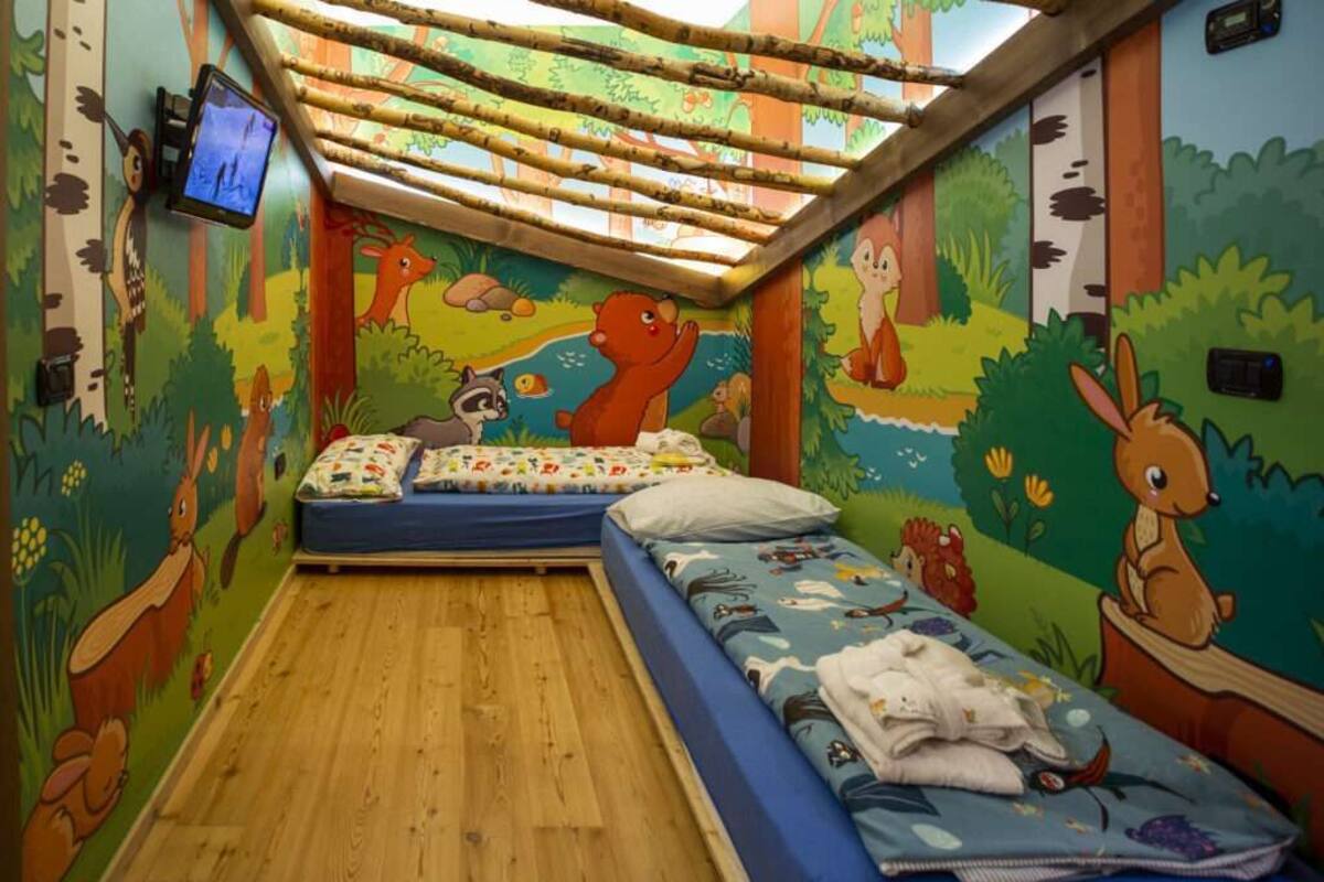 A children's room with two beds, a TV, and forest-themed wall art.