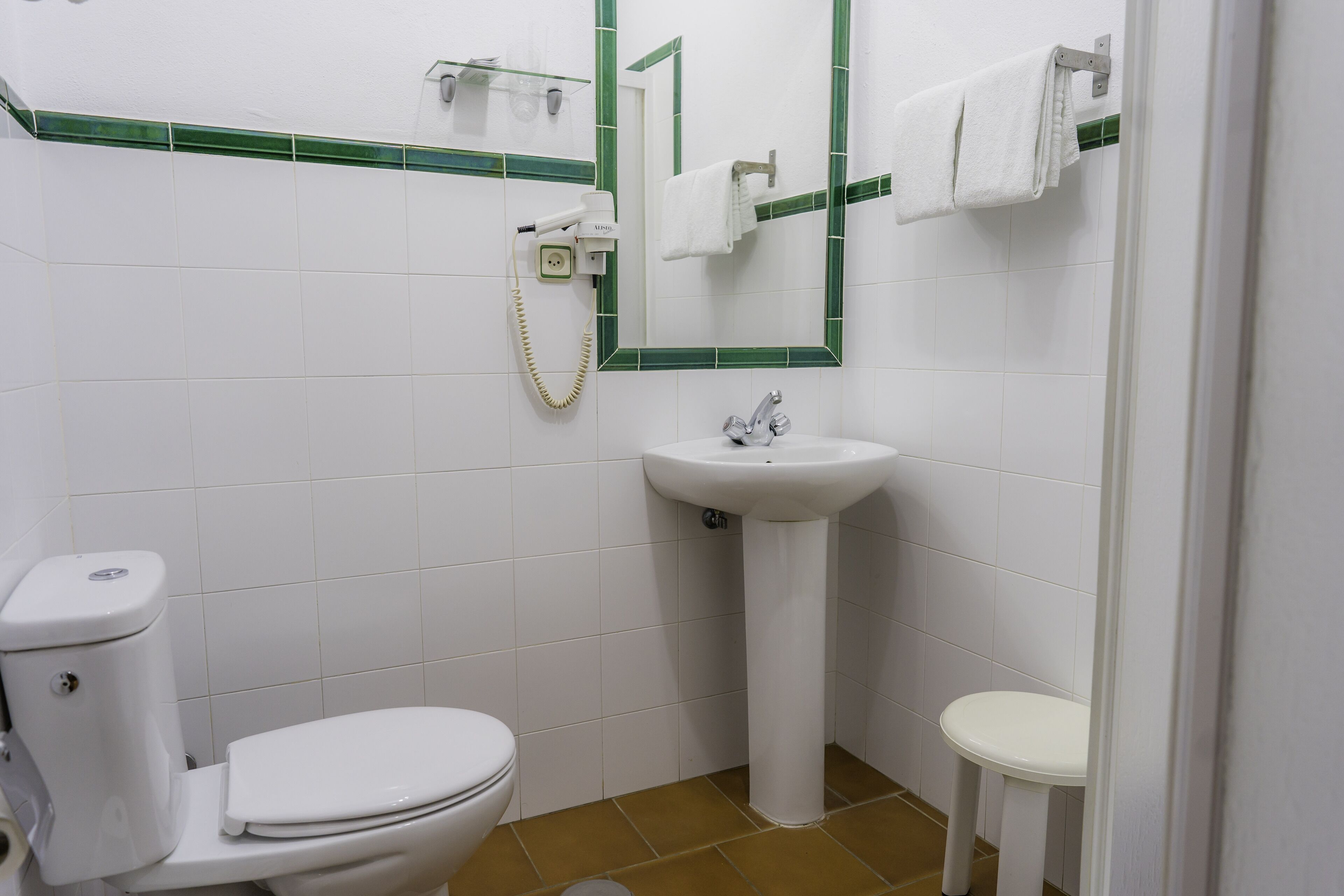 A bathroom with a toilet, sink, and a mirror with green tiles.
