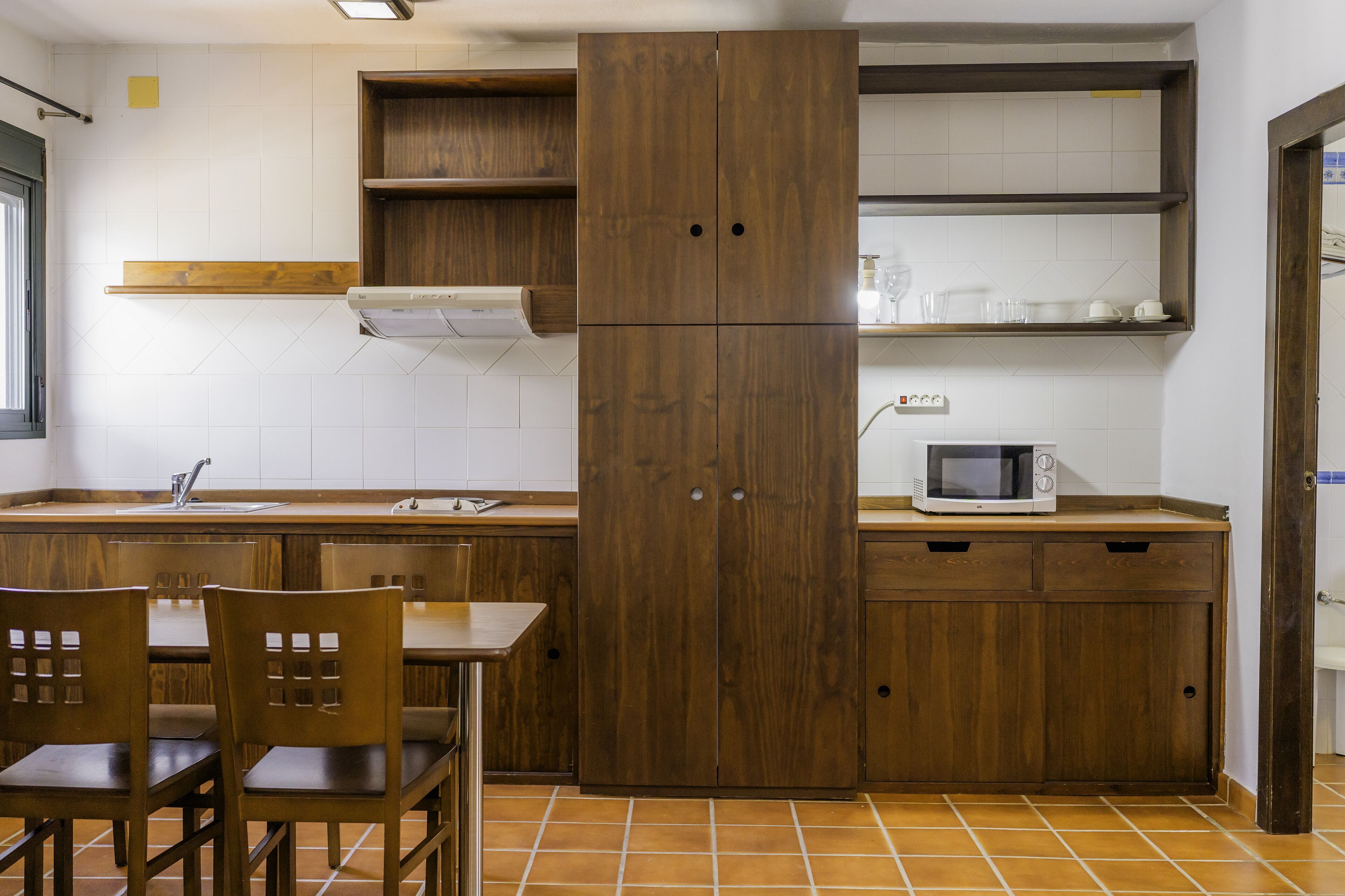 Una cocina con armarios de madera, un microondas y una zona de comedor con sillas.
