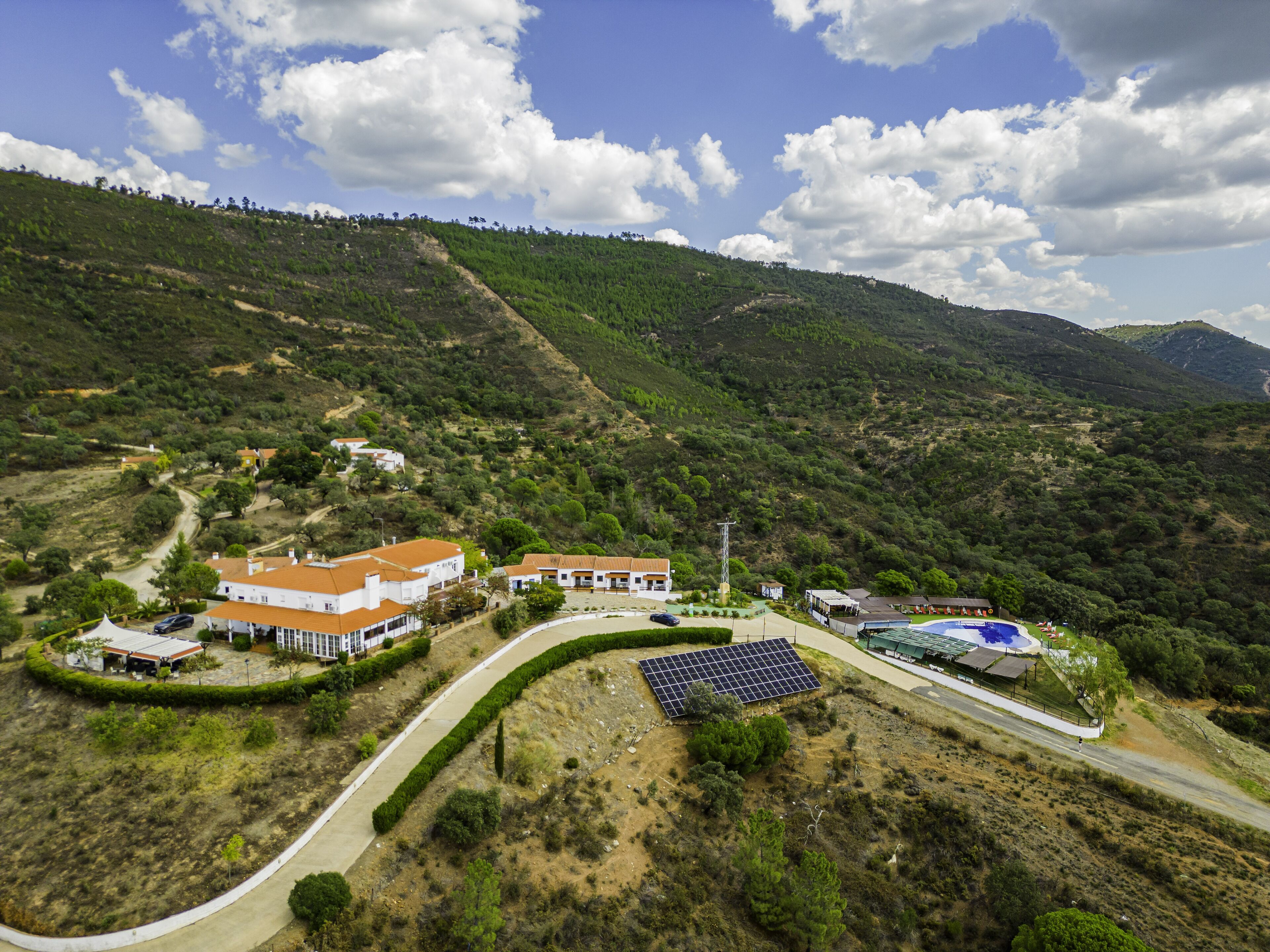 A hillside property with a winding road, solar panels, and a variety of buildings.