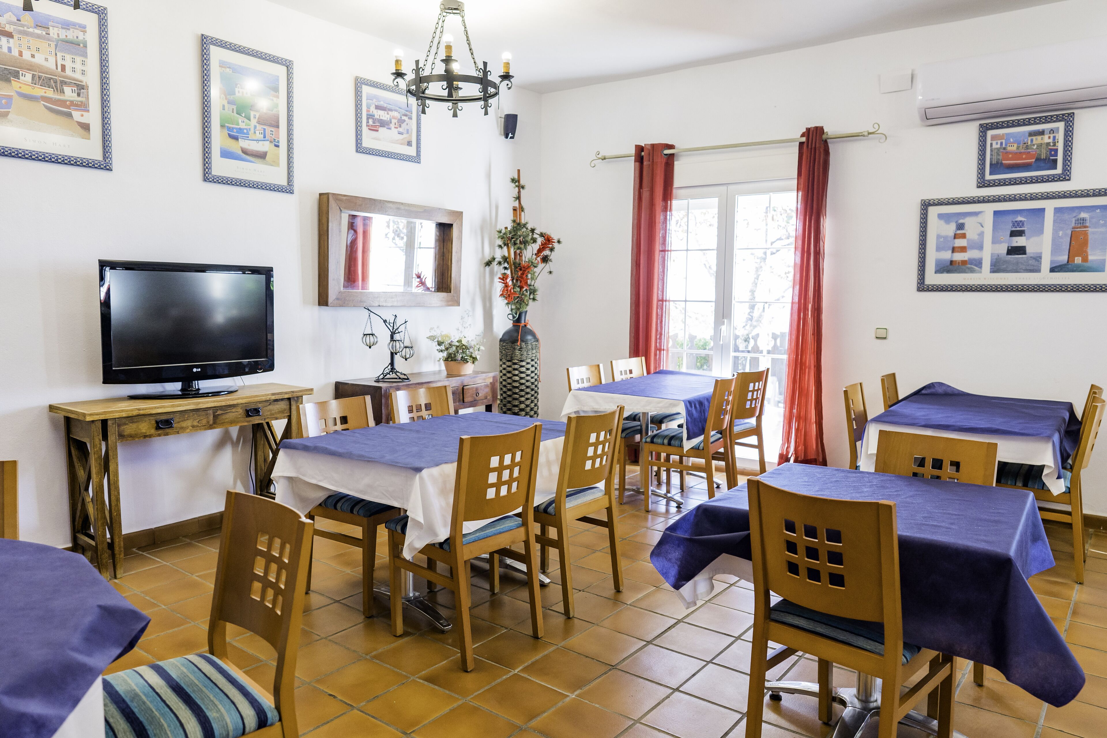A dining area with tables and chairs, a television, and framed pictures on the walls.