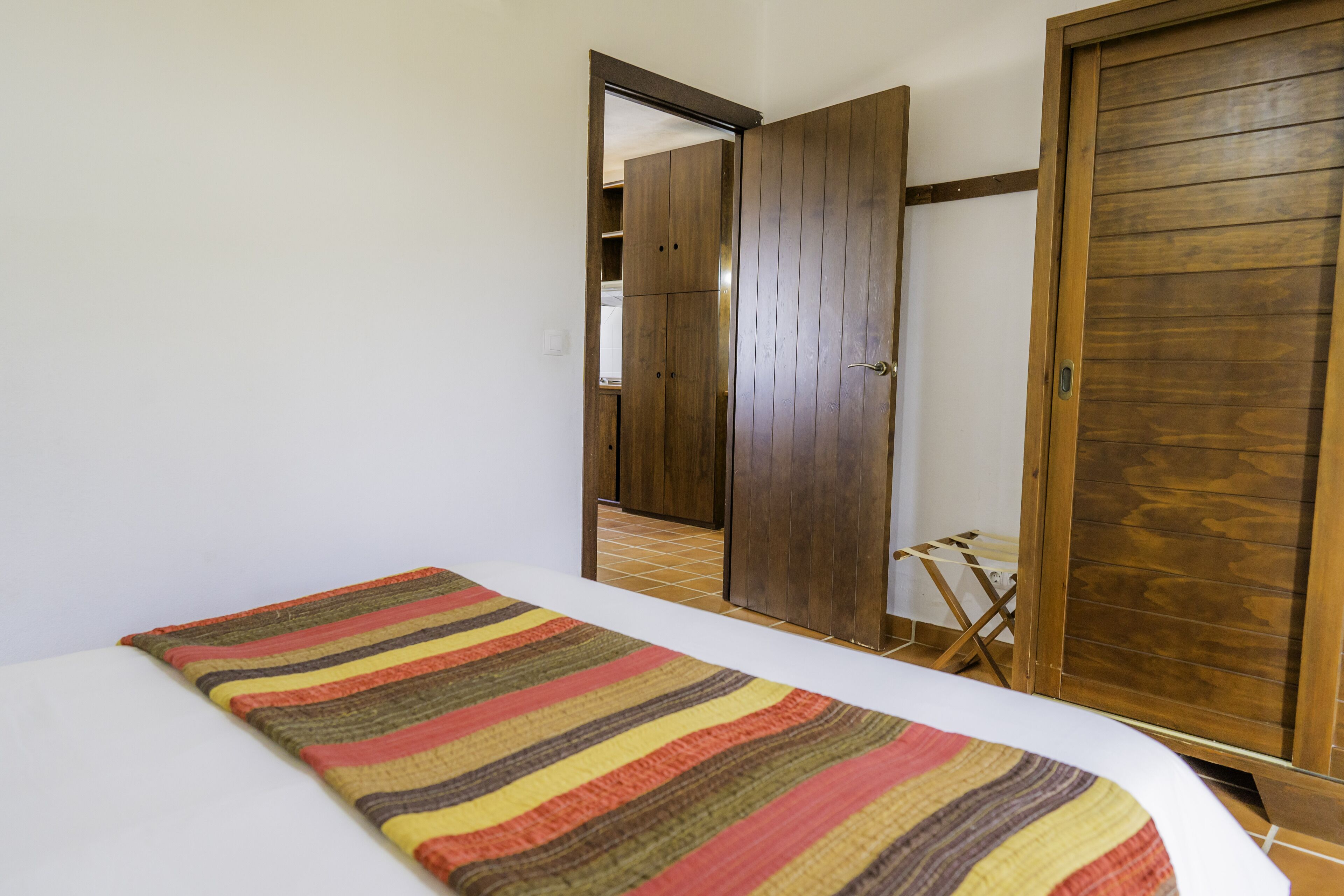 Habitación de hotel con una cama, alfombra a rayas, armario de madera y una puerta que da a otra habitación.