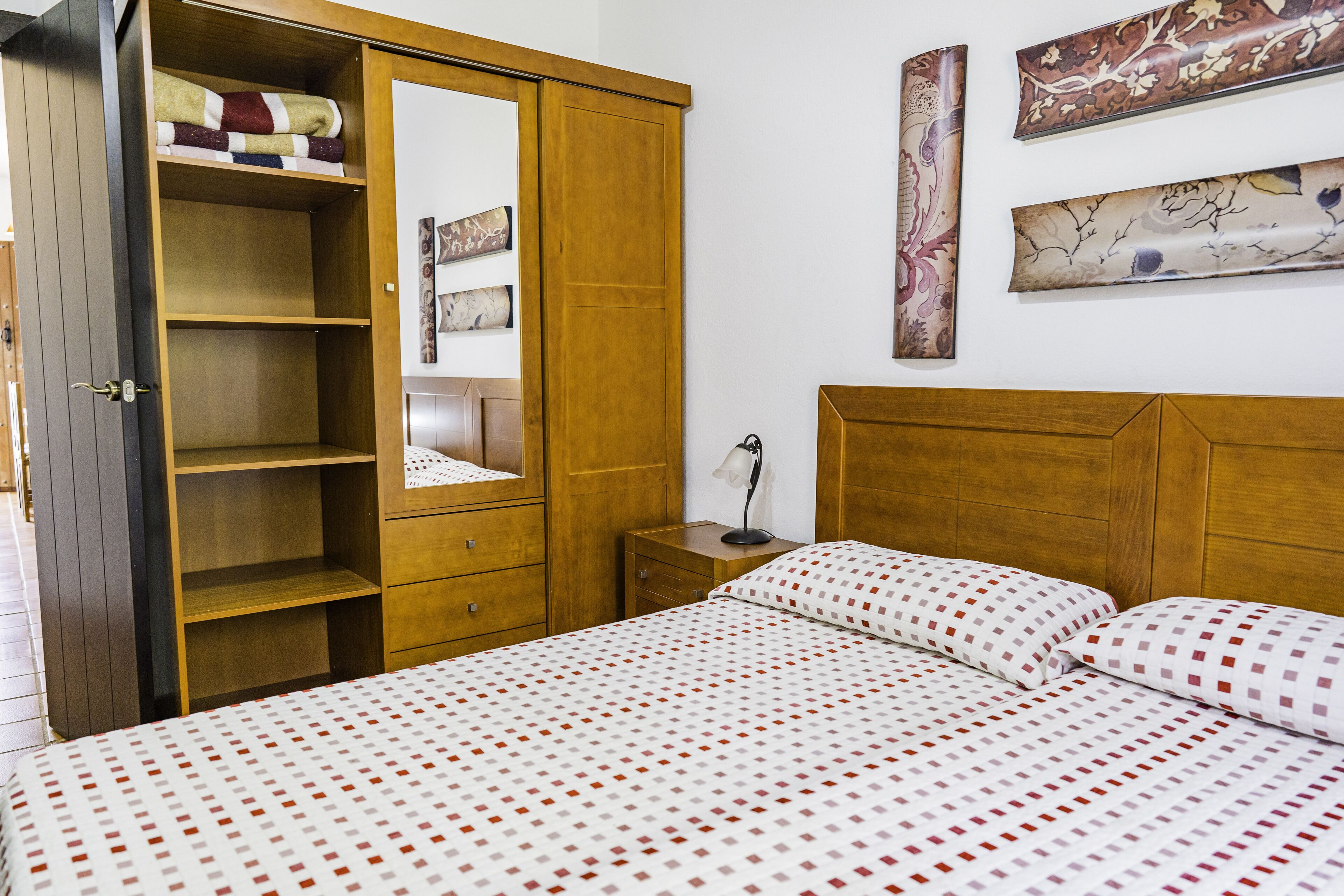 A bedroom with a bed, wooden wardrobe, and artwork on the wall.