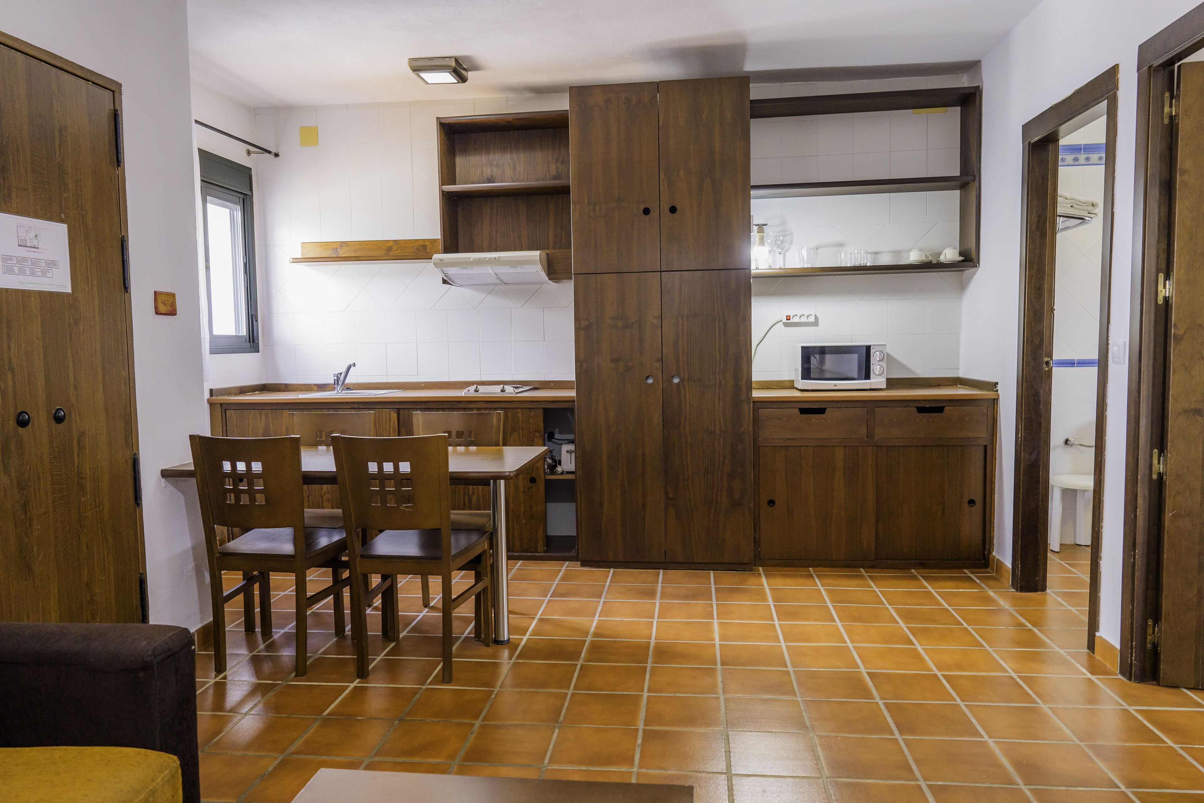 A compact kitchen with wooden cabinets, a microwave, and a dining area with chairs.