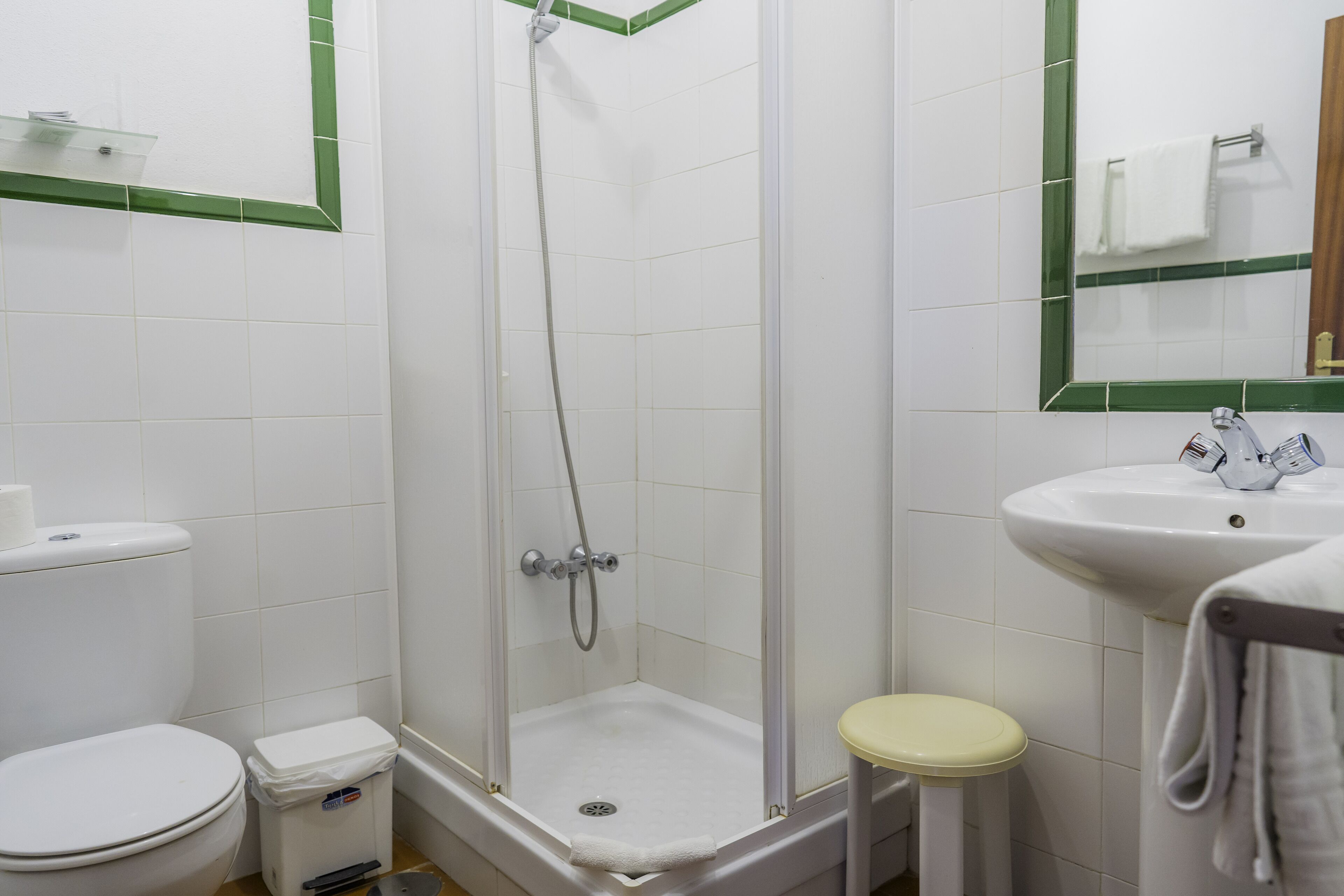 Baño con ducha, inodoro, lavamanos y espejo.