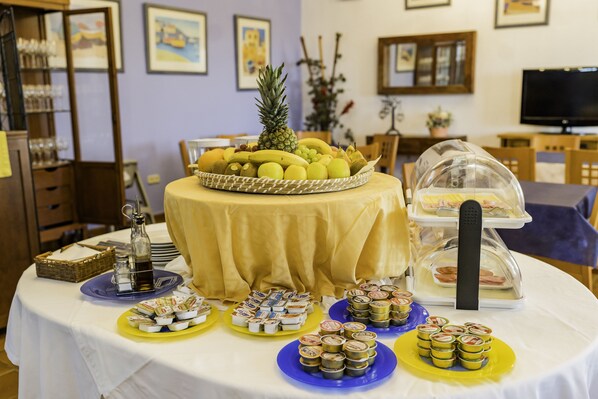 A buffet table with various food items, a pineapple centerpiece, and a television in the background. - Complejo Turístico Los Veneros (Santa Ana la Real)