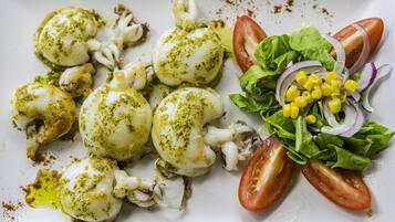 Un plato de comida con calamares, tomates, lechuga y maíz.