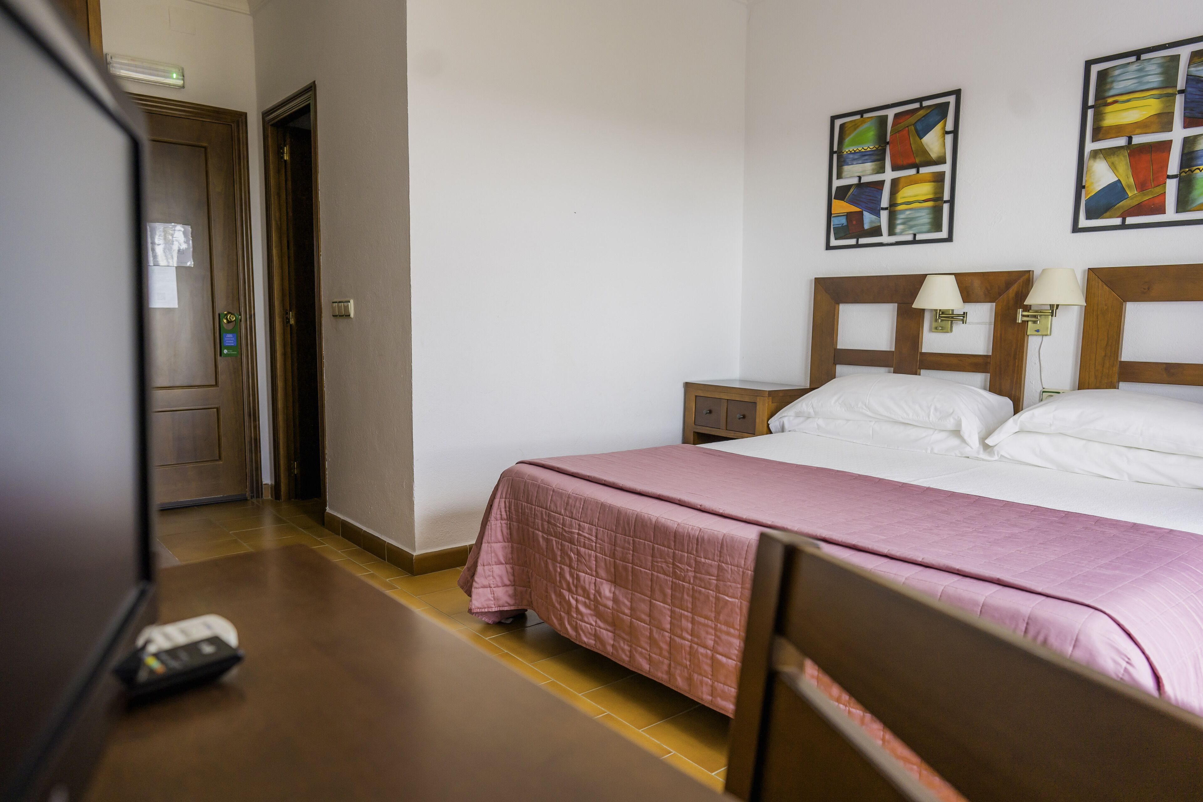 Una habitación de hotel con cama, mesita de noche, televisor y puerta.