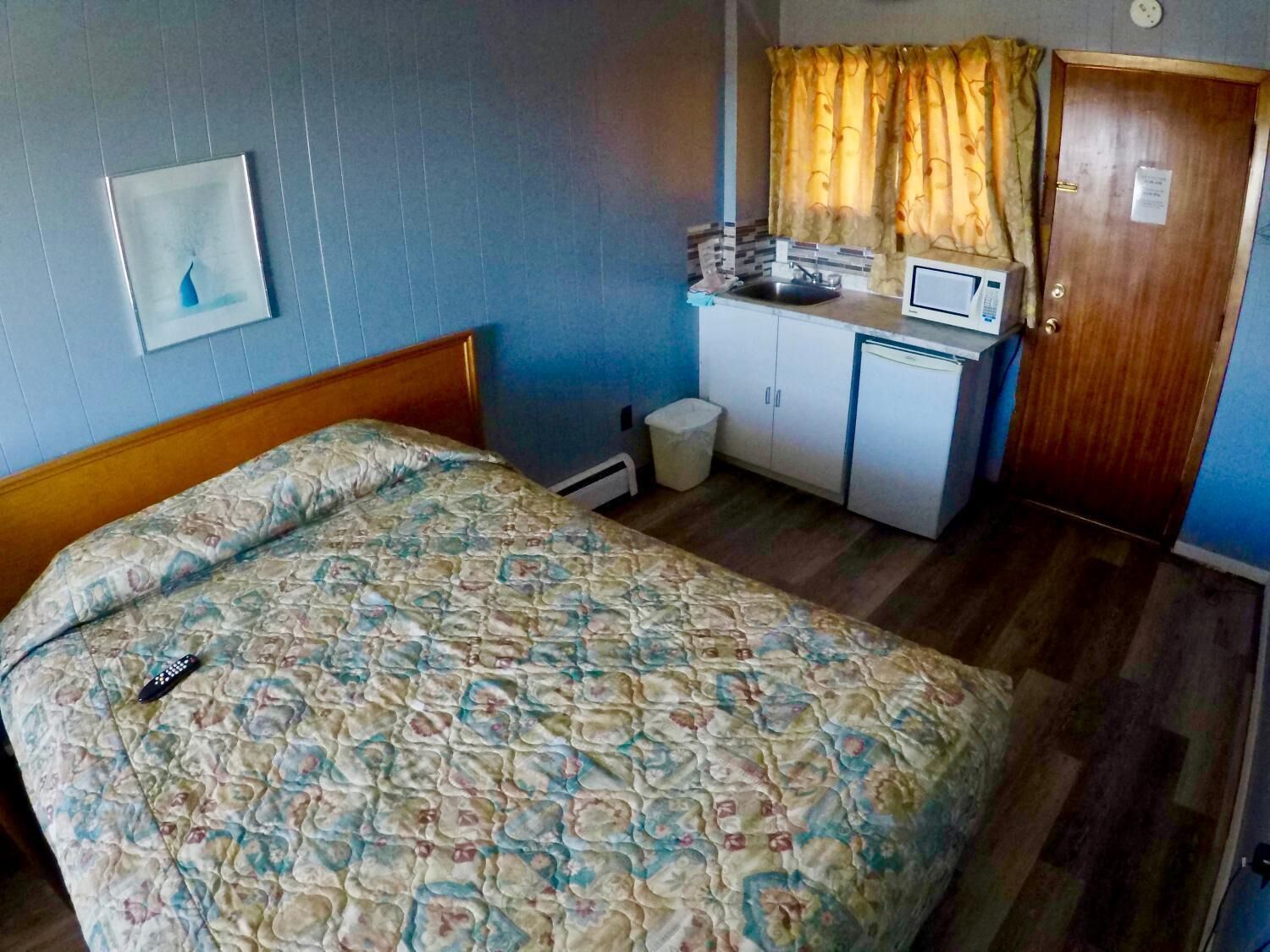 Una habitación con cama, una pequeña kitchenette, una puerta y un ventanal con cortinas.