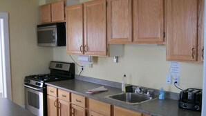 A kitchen with wooden cabinets, a microwave, a stove, a sink, and a toaster. - Hillside Motel (Saint John)